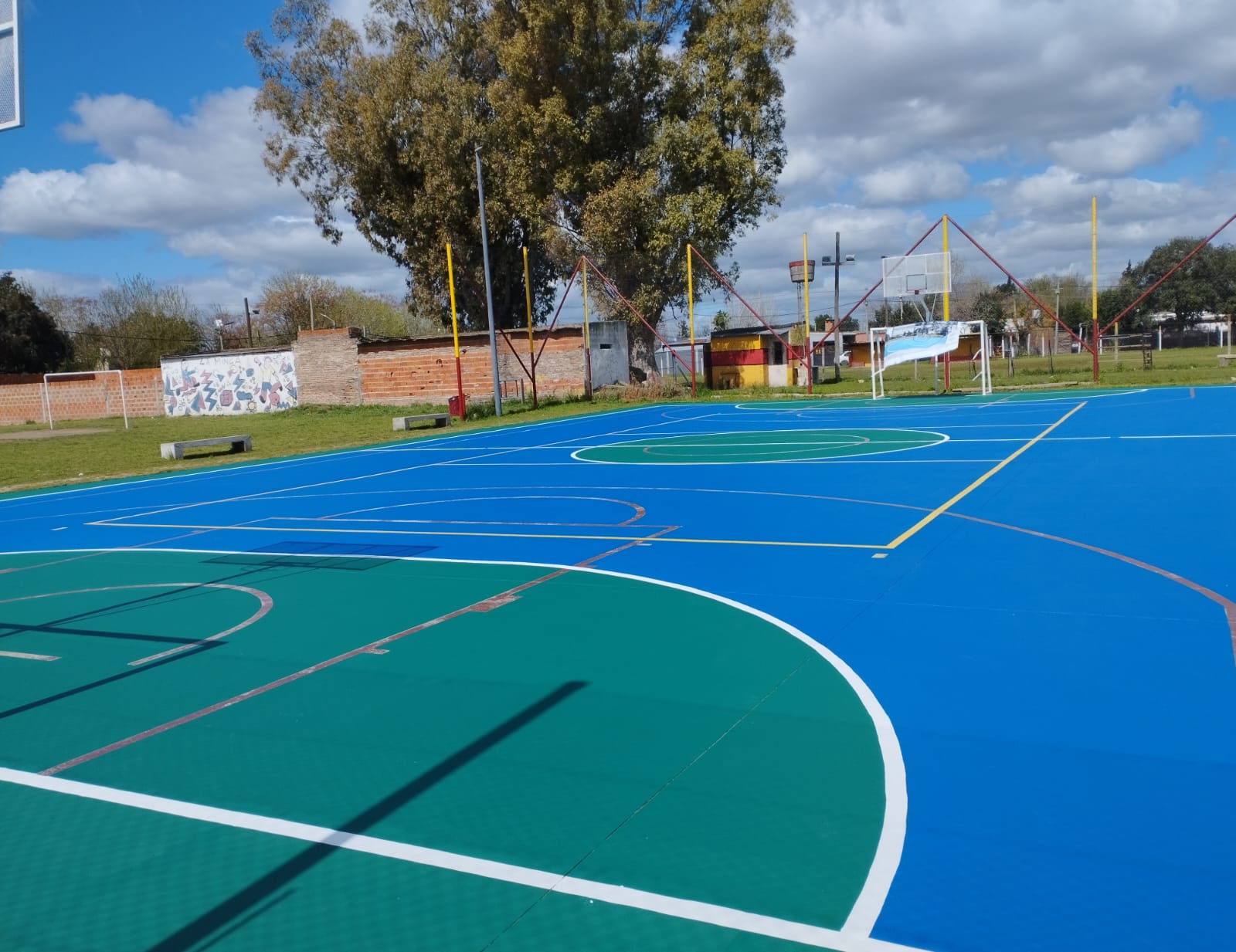 Cancha al aire libre pintada de azul y verde, con líneas de juego blancas y amarillas.